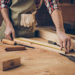closeup photo of cabinetmaker’s tabletop. Craftsman holding ruler on wooden planknear other tools